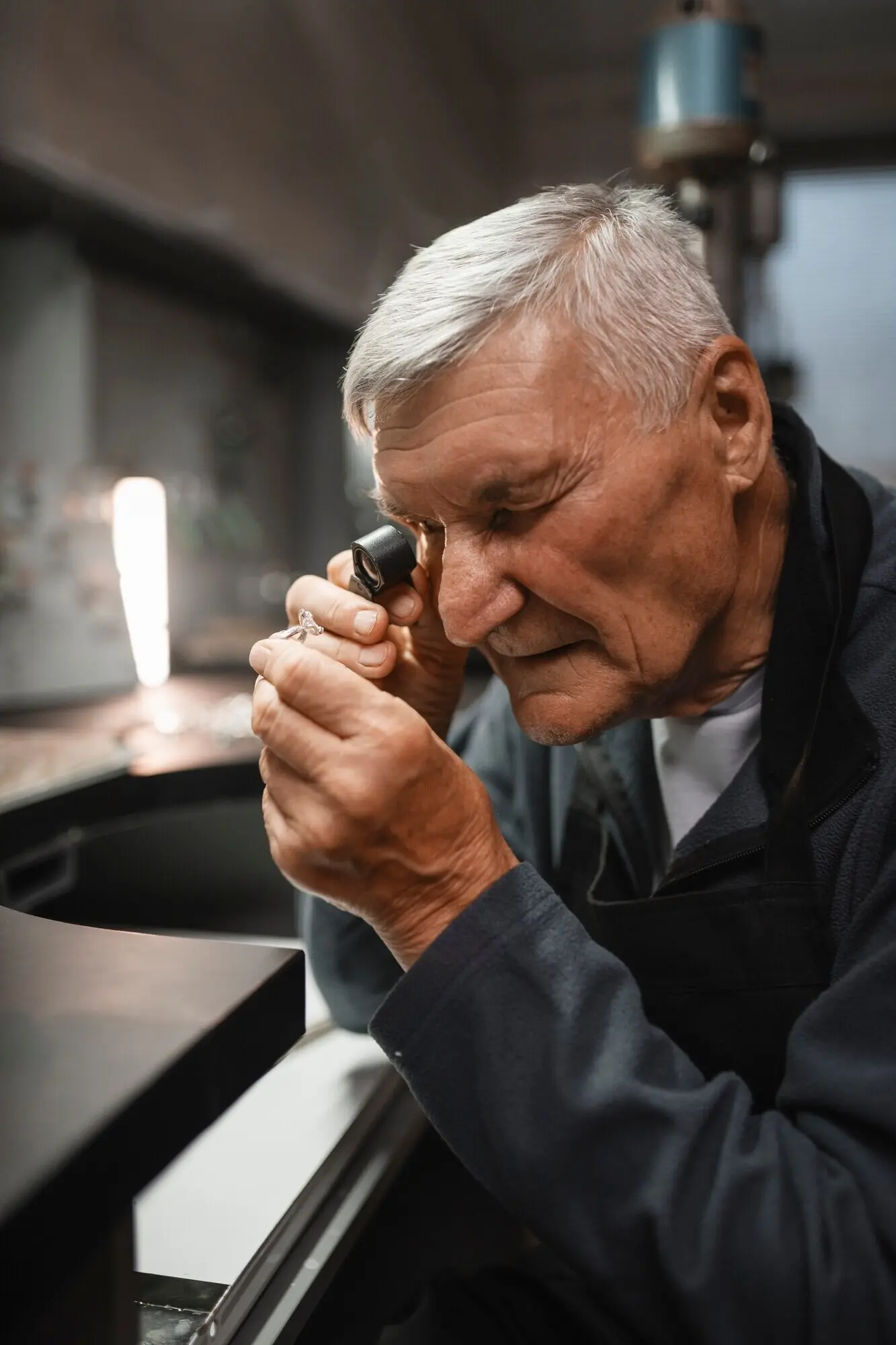 A male jeweler at work in the shop with a magnifying glass.